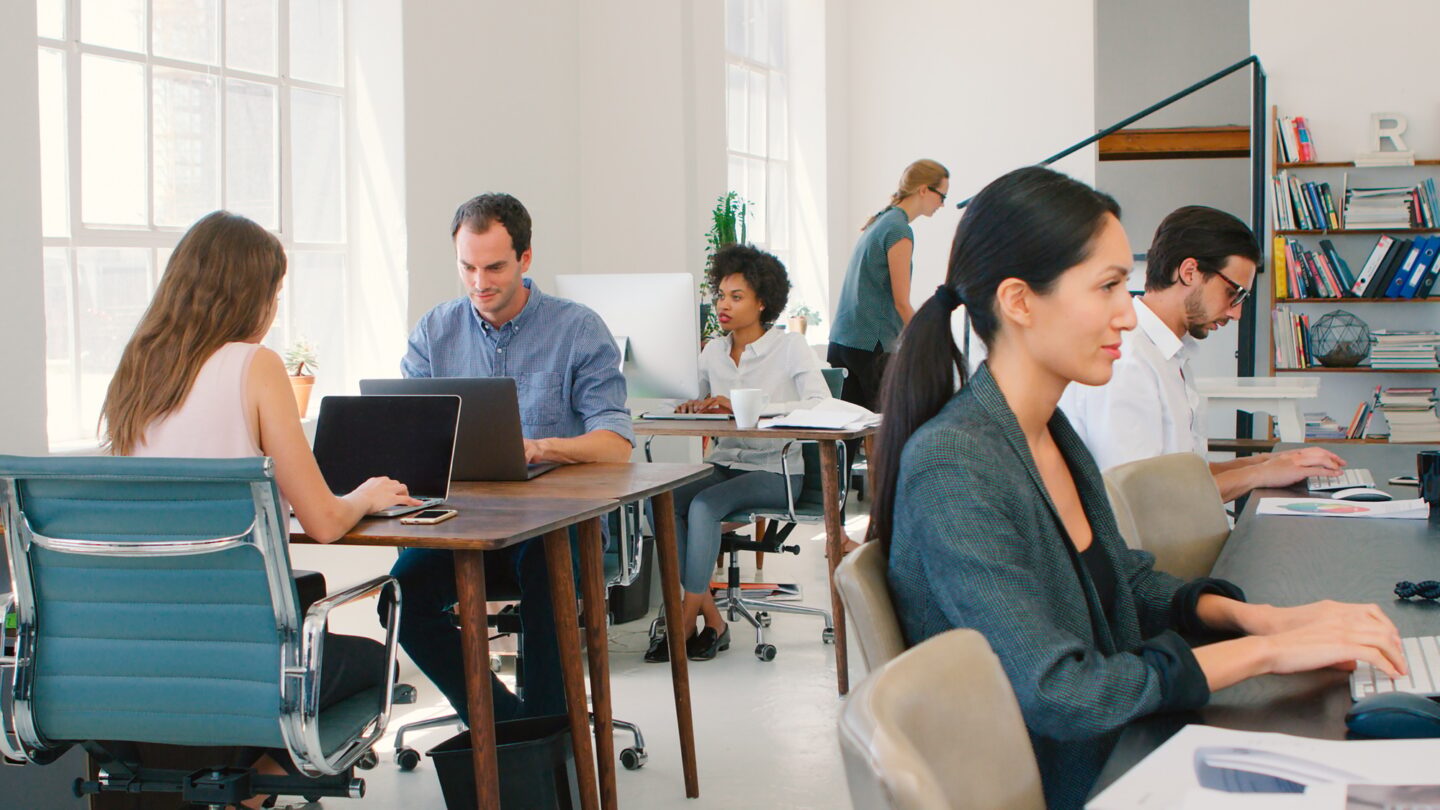 Multi-Cultural Business Team Working At Desks On Computers In Modern Open Plan Office