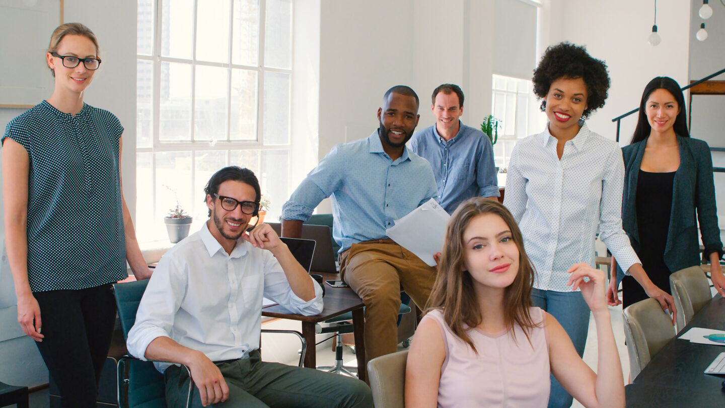 Portrait Of Multi-Cultural Business Team Working At Desks On Computers In Modern Open Plan Office