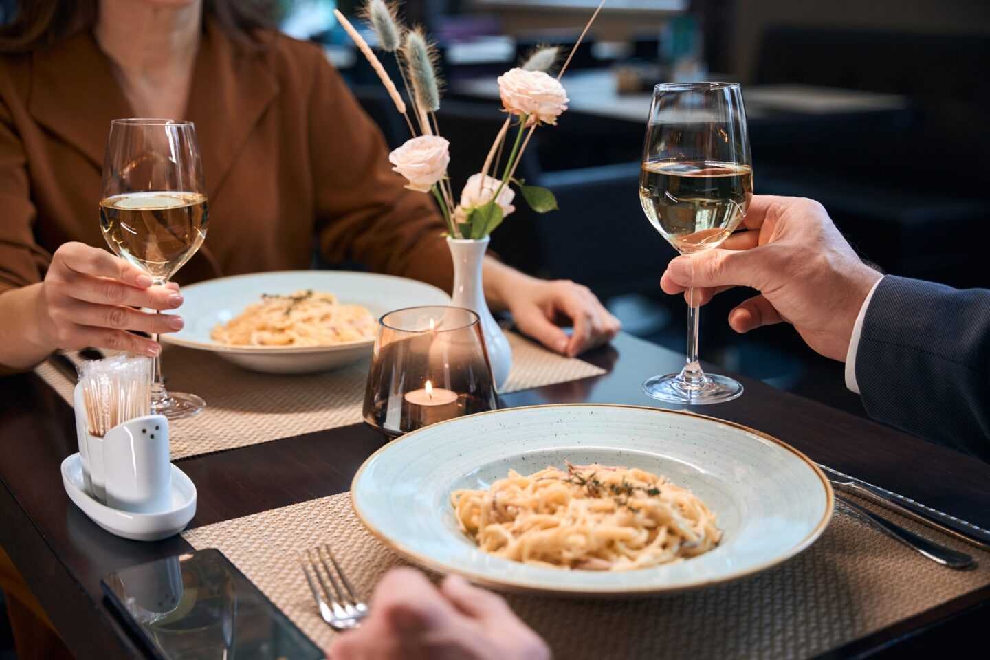 Cropped couple drinking wine from glasses and eating pasta in hotel restaurant