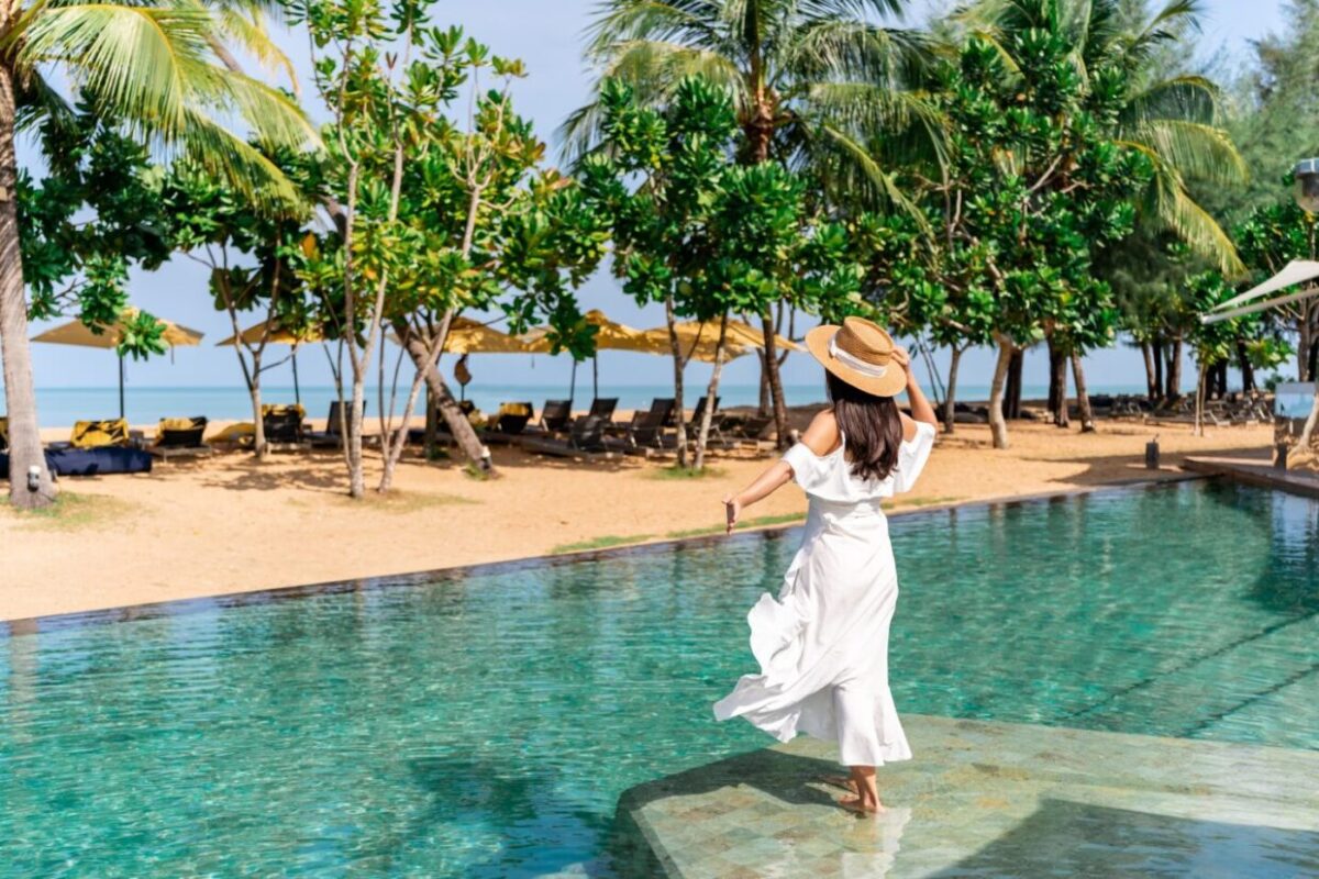 Young woman traveler relaxing and enjoying the beach view by a tropical resort pool while traveling