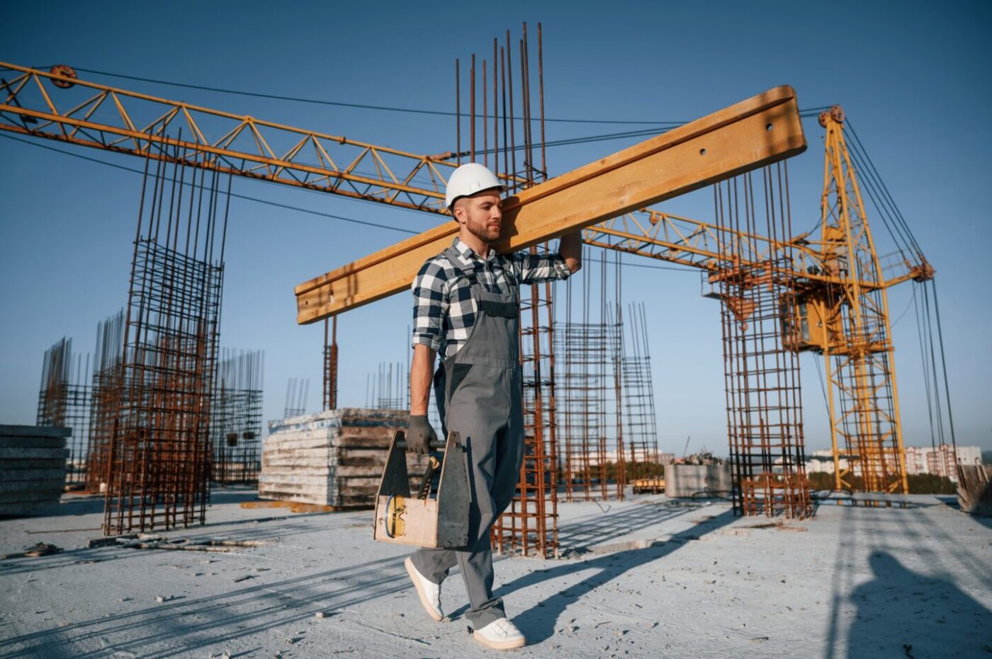 Holding big wooden piece. Man is working on the construction site at daytime